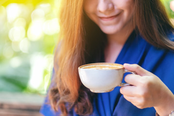 Closeup image of a beautiful asian woman holding and drinking hot coffee in the garden