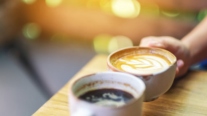 Close up image of two people clinking coffee mugs on wooden table
