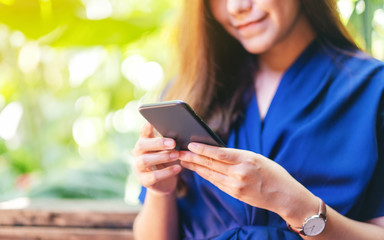 Closeup image of a beautiful asian woman holding , using and looking at mobile phone in the garden