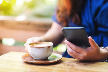 Closeup image of a woman holding and using mobile phone while drinking coffee in the garden