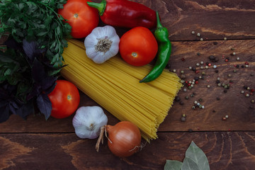 a bunch of spaghetti with vegetables, onions, garlic, bell peppers, chili peppers, tomatoes with a bunch of parsley and Basil, Regan, and scattered spices and Bay leaf top view