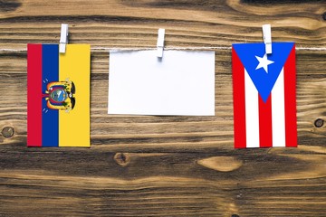 Hanging flags of Ecuador and Puerto Rico attached to rope with clothes pins with copy space on white note paper on wooden background.Diplomatic relations between countries.