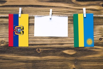 Hanging flags of Ecuador and Rwanda attached to rope with clothes pins with copy space on white note paper on wooden background.Diplomatic relations between countries.