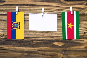 Hanging flags of Ecuador and Suriname attached to rope with clothes pins with copy space on white note paper on wooden background.Diplomatic relations between countries.