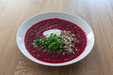 White plate of beetroot soup with parsley and sunflower seeds. Vegetarian dish, fresh soup.