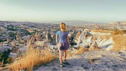 Naklejka premium View from the back of a girl stands on a hill and looks at synset in Cappadocia, Turkey.