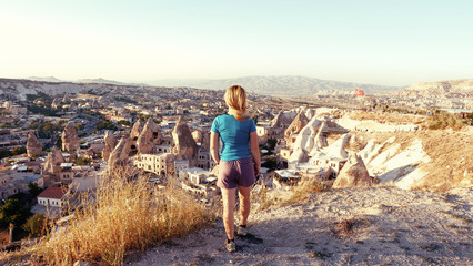 View from the back of a girl stands on a hill and looks at synset in Cappadocia, Turkey.