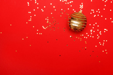 Christmas composition greeting card. Christmas golden ball on a red background with a gold star confetti. Top view, flat lay. Minimalist concept