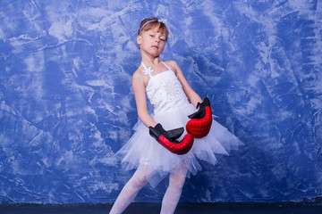 Beautiful little girl in a white dress and boxing gloves on a blue background.