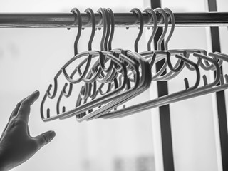 Black and white tone of woman 's hand and stack of clothes hanger hang on aluminum clothesline, prepare for drying after laundry or washing process.
