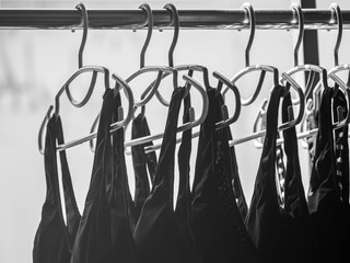 Black and white tone of stack of clothes hanger hang on aluminum clothesline with black sports bras for drying after laundry or washing process.