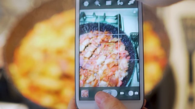 Close-up girl takes pictures on a smartphone delicious food, which is fried and steaming in a frying pan meat with vegetables. American lunch, dinner.