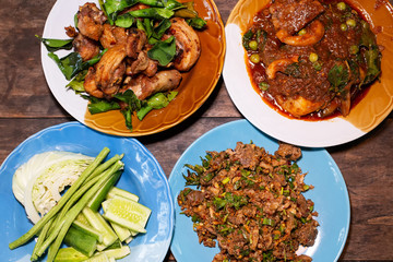 Spicy food in wood table such as Duck minced salad (Larb Ped), Deep fried chicken, Stir fried fish with red chili paste on wood table. Thai traditional local food style dining table top view.