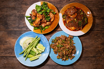 Spicy food in wood table such as Duck minced salad (Larb Ped), Deep fried chicken, Stir fried fish with red chili paste on wood table. Thai traditional local food style dining table top view.