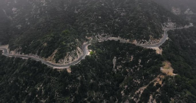 Drone shot winding road in wooded mountains under foggy haze (Santa Anita Canyon, California, USA)