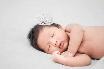 Newborn baby boy sleeping and wearing a silver crown.