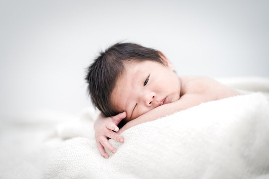 Happy cute adorable Asian baby boy with black hair lying on a white bed.