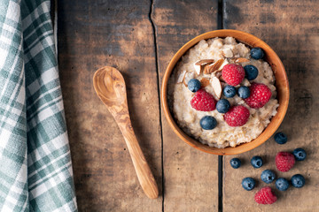 Overhead/Flat lay food photography shot of oakmeal with berries and wooden spoon, green linen laying on table. Healthy, lifestyle and fitness concept.