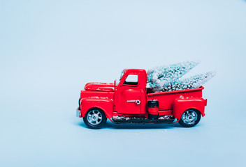 Red truck car carrying a Christmas fir tree with garland on the snow blue background. Concept for magic fairytale Merry Christmas and Winter holidays. Copy space Place text. Snow bokeh