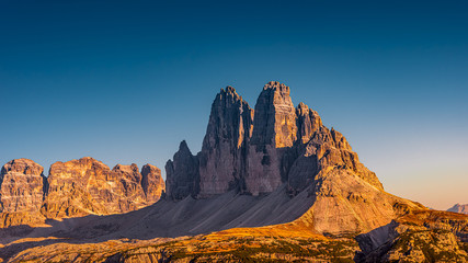 Panoramic view over beautiful sunset in magical Three Dolomite peaks at the national park Three Peaks (Tre Cime, Drei Zinnen) in Autumn October colors at blue sky, South Tyrol, Italy © neurobite