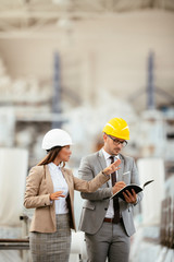 Businessman and businesswoman in factory. Man and woman in suits with helmets in factory discussing work.