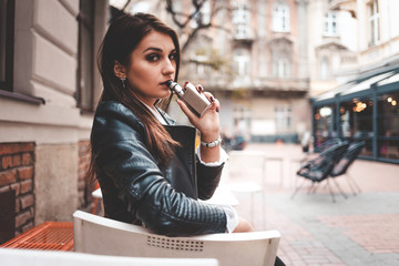 Stylish girl smokes a electronic cigarette. Serious woman with vape sitting on the table