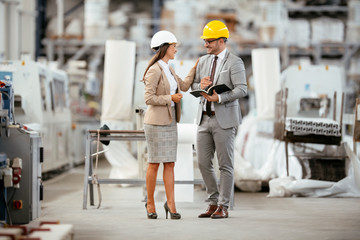 Businessman and businesswoman in factory. Man and woman in suits with helmets in factory discussing work.