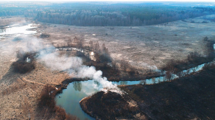 Forest and field fire. Dry grass burns, natural disaster. Aerial view. Smooth flight over the place of fire, a small stream blocks the path to the fire.