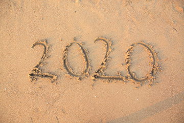 020 text painted on the yellow sand on the beach.