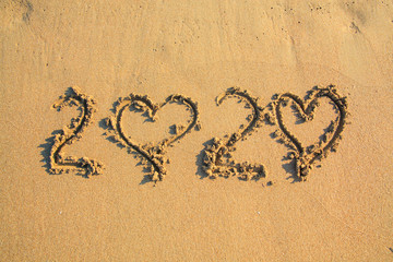020 text painted on the yellow sand on the beach.