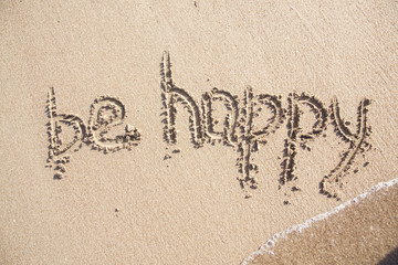 Word be HAPPY drawn on the sand of sandy beach.