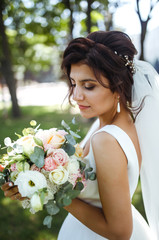 Beautiful bride with a wedding bouquet for a walk in the park. Young bride in white dress. Beautiful woman with professional make up and hair style. A beautiful bride portrait. Wedding day. Marriage.