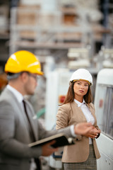 Businessman and businesswoman in factory. Man and woman in suits with helmets in factory discussing...