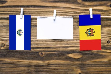 Hanging flags of El Salvador and Moldova attached to rope with clothes pins with copy space on white note paper on wooden background.Diplomatic relations between countries.