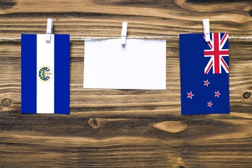 Hanging flags of El Salvador and New Zealand attached to rope with clothes pins with copy space on white note paper on wooden background.Diplomatic relations between countries.