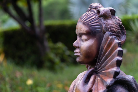 Side view of the face of a woman statue wearing kimono and holding a fan in her hands. Buddhism and inner peace concept