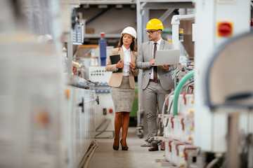 Businessman and businesswoman in factory. Man and woman in suits with helmets in factory discussing...