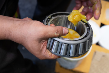 Senior worker putting lubricant lithium grease (NLGI 3) into wheel bearing for ten wheel truck car by hand at service station in Asia. Grease appearance is yellow. Maintenance and preventive concept.  - obrazy, fototapety, plakaty