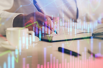 Double exposure of man's hands writing notes of stock market with forex chart.