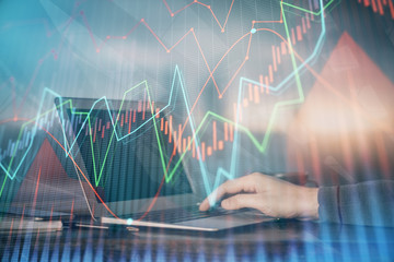 Double exposure of businessman's hands with laptop and stock market graph background. Concept of research and trading.