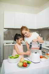 Mother and Daughter are preparing the salad in blender Menu tasty smoothie and ingredients on table at home