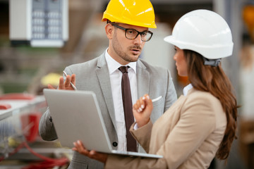 Businessman and businesswoman in factory. Man and woman in suits with helmets in factory discussing work.