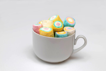Multi-colored marshmallows in a white tea cup on a white background