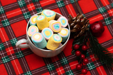 Multi-colored marshmallows in a white tea cup on a checkered napkin. Christmas decor, holiday.