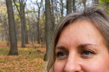Face closeup of middle aged woman in autumn forest. Girl does not look at camera and smiles on blurred background. Thought, meditation or doubt expression. Relax or other mental psychology concept