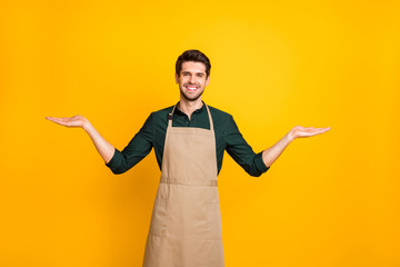 Photo of cheerful positive attractive kind friendly coffee maker showing you to kinds of one sort object of coffee smiling toothily wearing apron isolated over yellow vivid color background