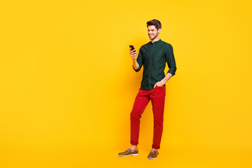 Full size photo of positive cheerful guy have fun on spring holidays use his smartphone typing post comment follow blogs wear casual style outfit sneakers isolated over yellow color background