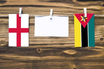 Hanging flags of England and Mozambique attached to rope with clothes pins with copy space on white...