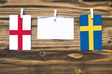 Hanging flags of England and Sweden attached to rope with clothes pins with copy space on white note paper on wooden background.Diplomatic relations between countries.