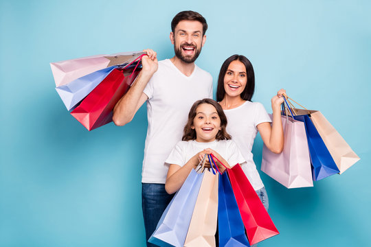 Portrait of excited positive cheerful three people mommy daddy schoolkid with brown hair shop center hold bags wear white t-shirt denim jeans isolated over blue color background